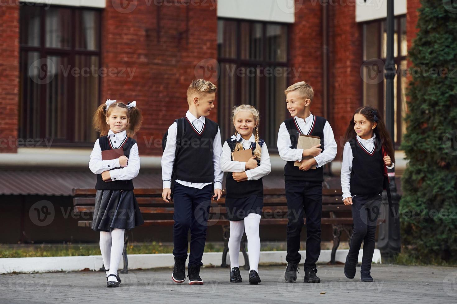 grupo de niños con uniforme escolar que están juntos al aire libre cerca del edificio de educación foto