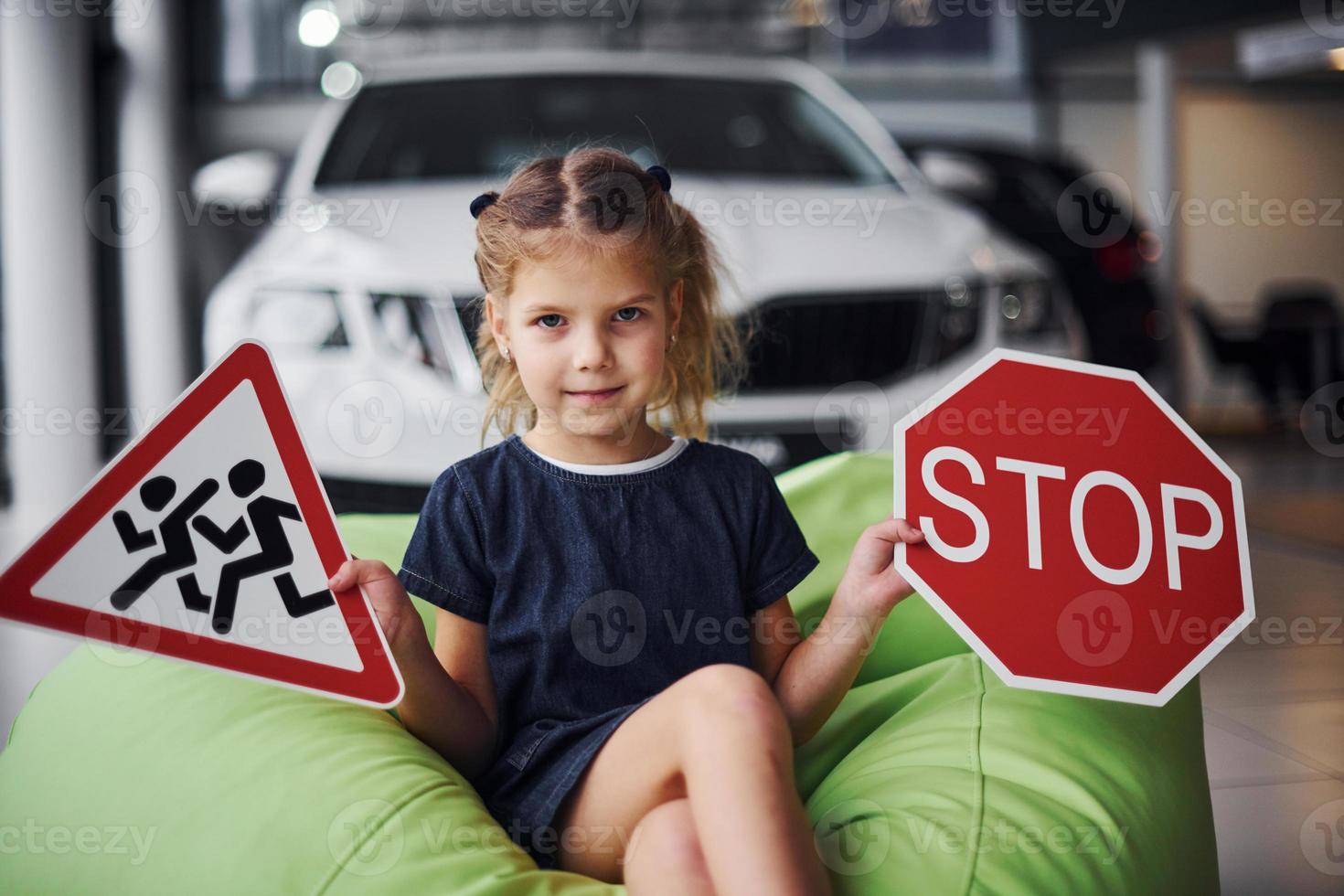 Portrait of cute little girl that holds road signs in hands in automobile salon photo