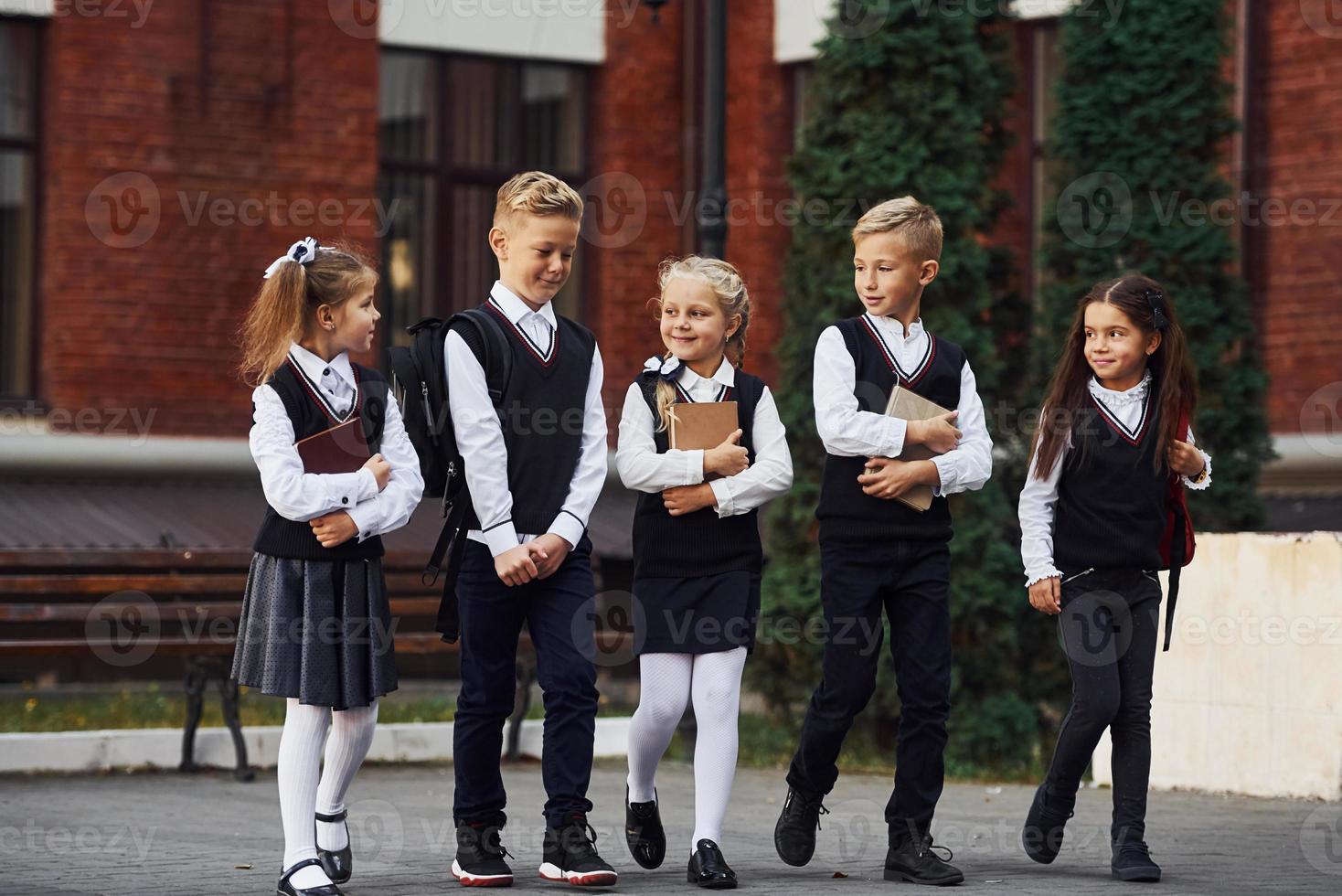 grupo de niños con uniforme escolar que están juntos al aire libre cerca del edificio de educación foto