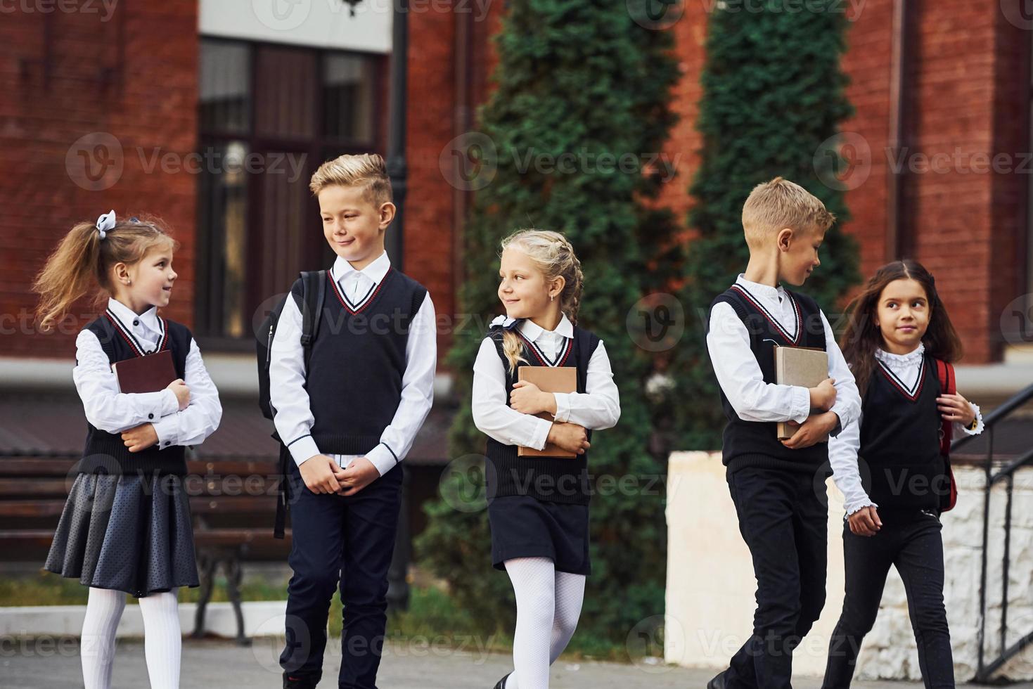 grupo de niños con uniforme escolar que están juntos al aire libre cerca del edificio de educación foto