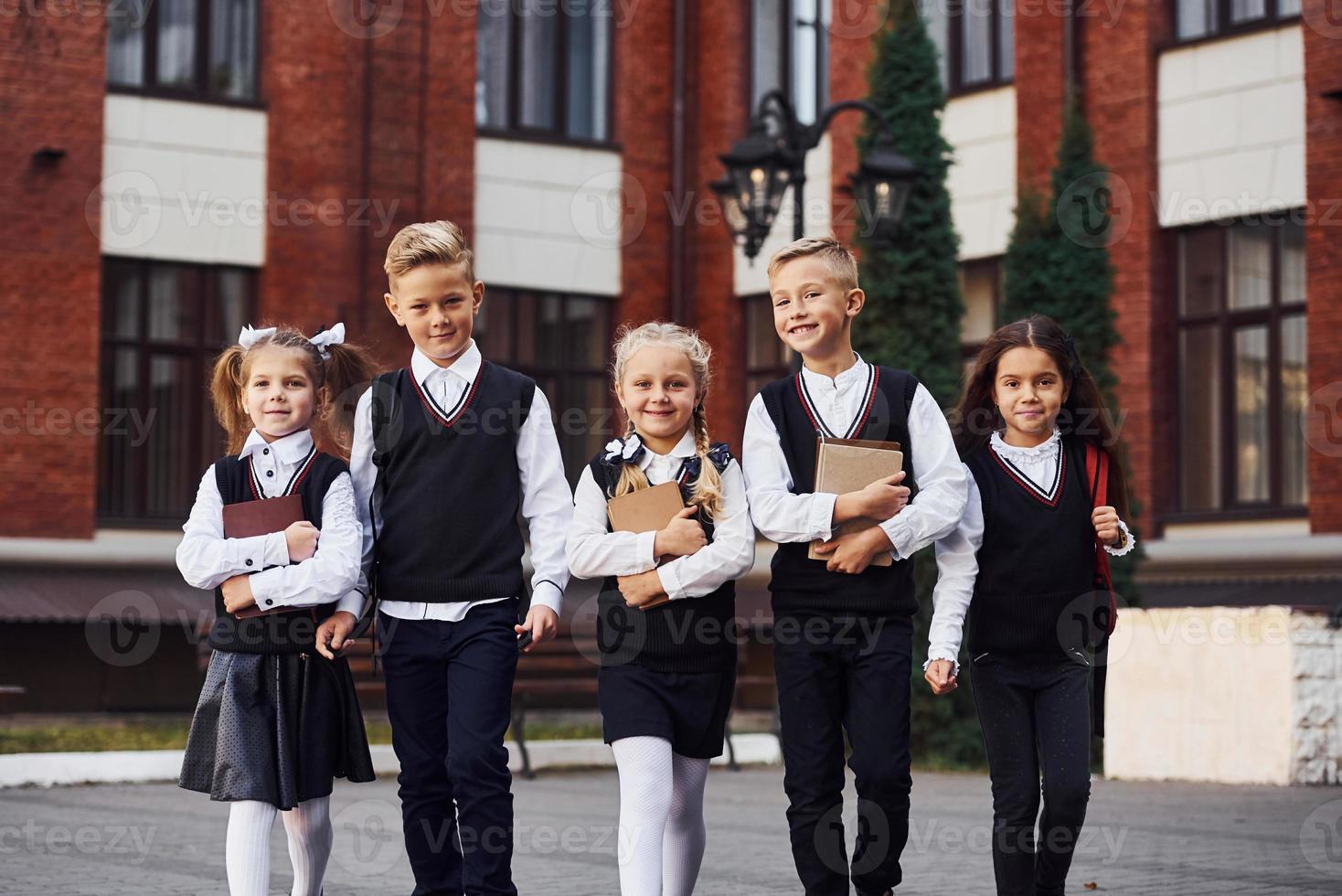 grupo de niños con uniforme escolar que están juntos al aire libre cerca del edificio de educación foto