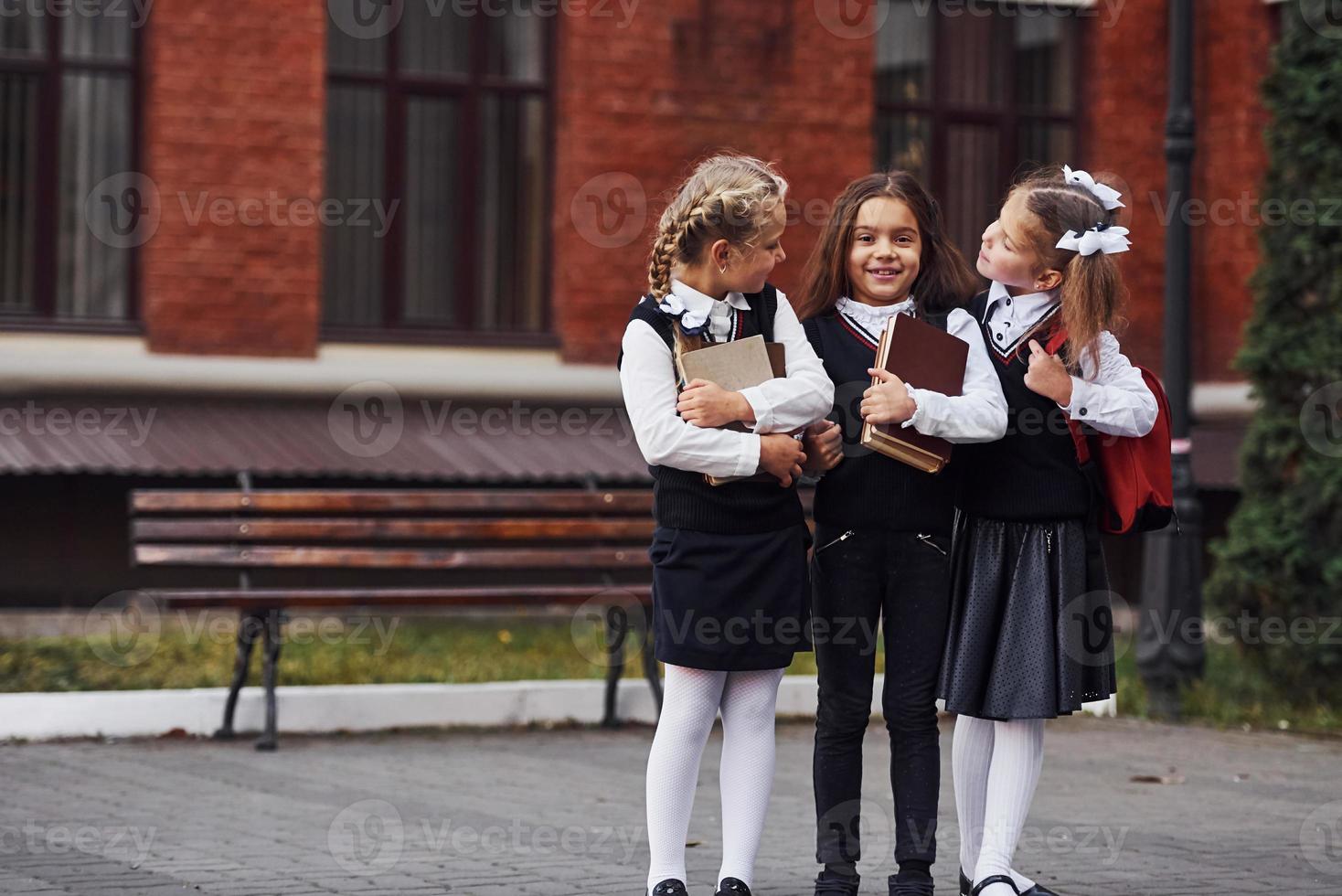 grupo de niñas con uniforme escolar que están juntas al aire libre cerca del edificio de educación foto