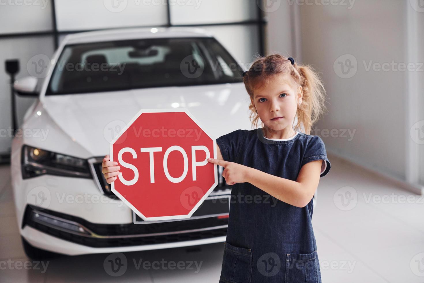 Portrait of cute little girl that holds road sign in hands in automobile salon photo