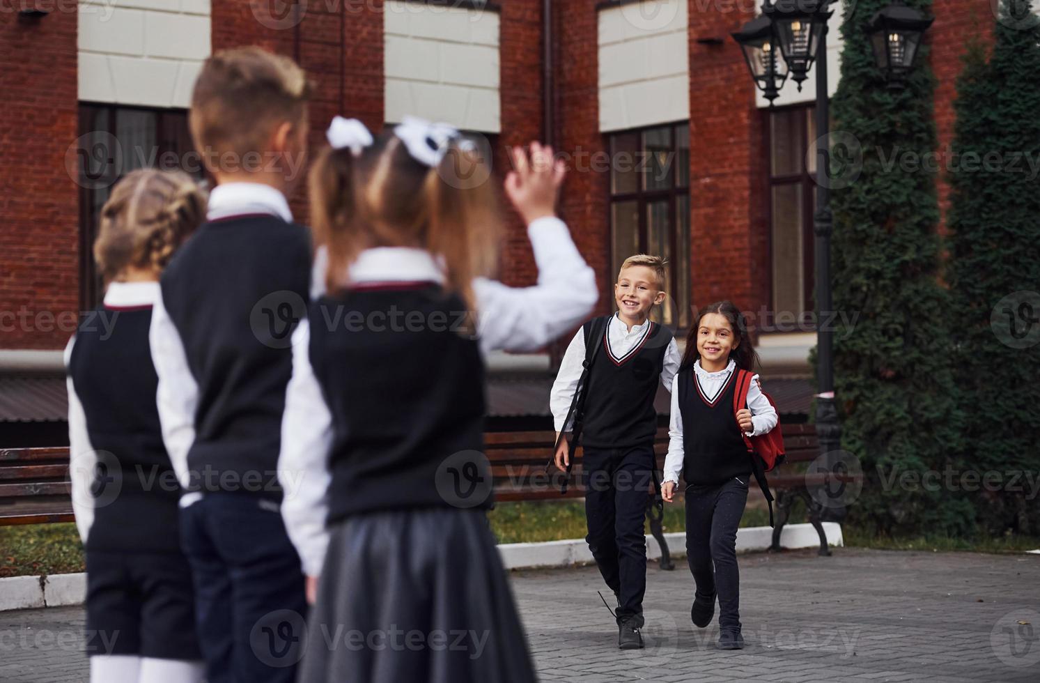 tener una reunión. grupo de niños con uniforme escolar que están juntos al aire libre cerca del edificio de educación foto