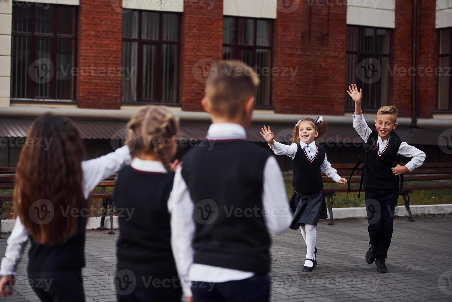 tener una reunión. grupo de niños con uniforme escolar que están juntos al aire libre cerca del edificio de educación foto