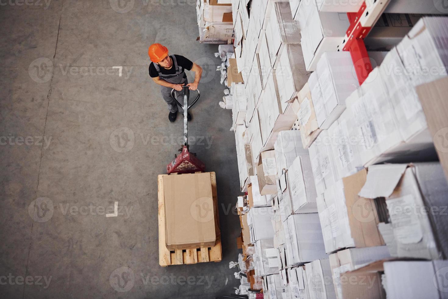 Top view of young male worker in uniform that is in the warehouse pushing pallet truck photo