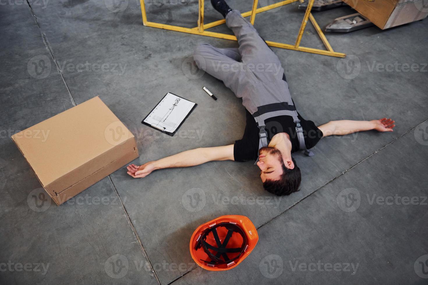 Warehouse worker after an accident in the storage. Man in uniform lying down on the ground photo