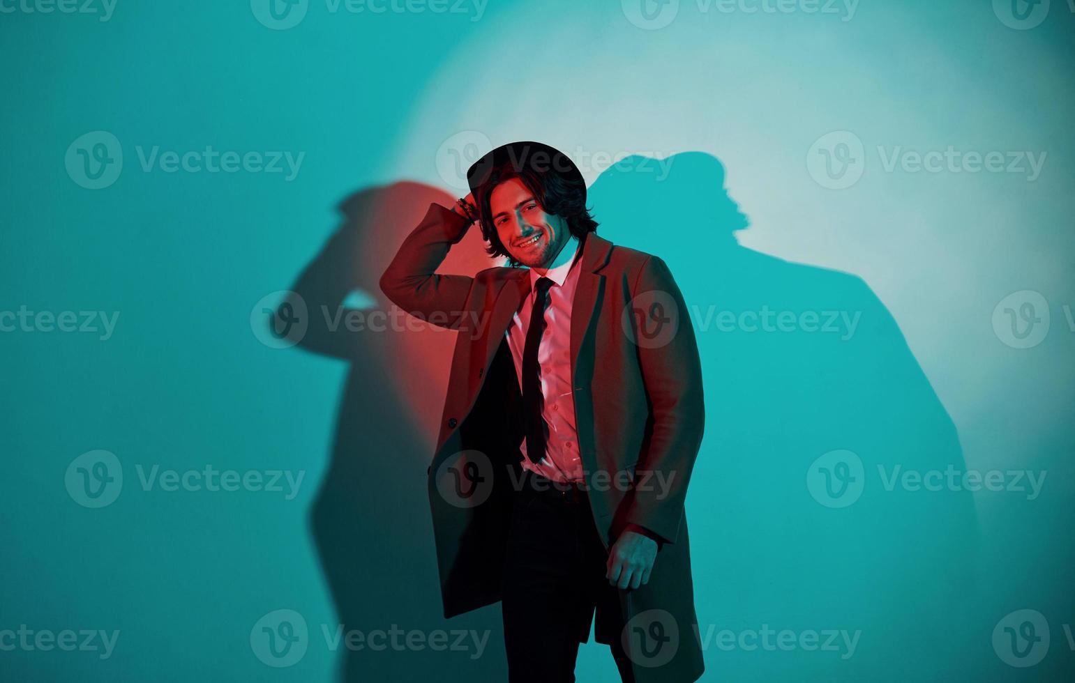 Portrait of young stylish man in hat, suit and tie that stands in neon lights in the studio photo