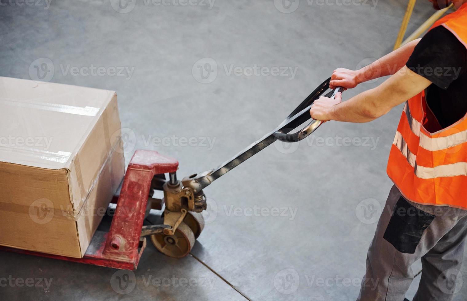 Young male worker in uniform is in the warehouse pushing pallet truck photo