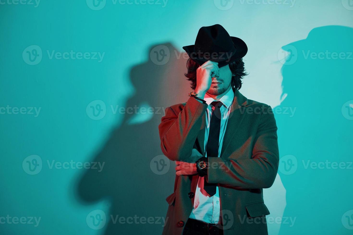 Portrait of young stylish man in hat, suit and tie that stands in neon lights in the studio photo