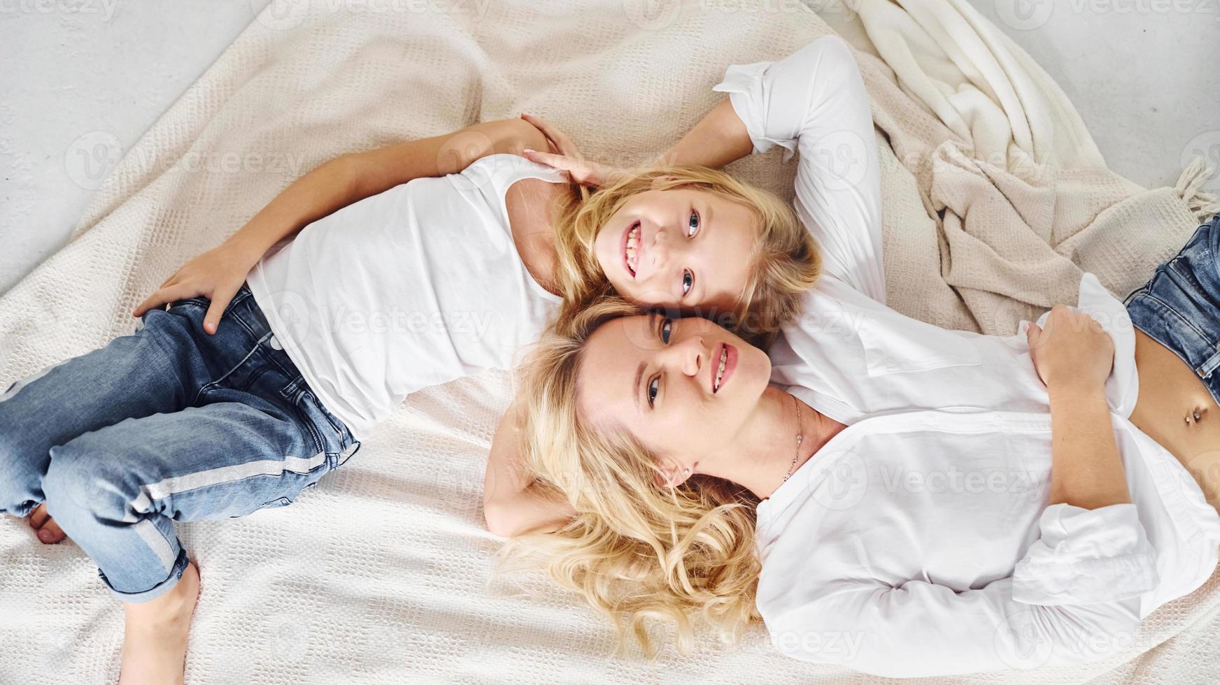 Mother with her daughter lying down together on the white bed photo