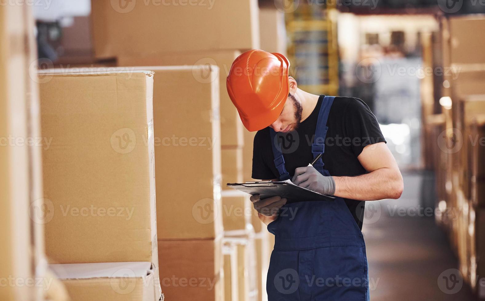 Storage worker in uniform and notepad in hands checks production photo