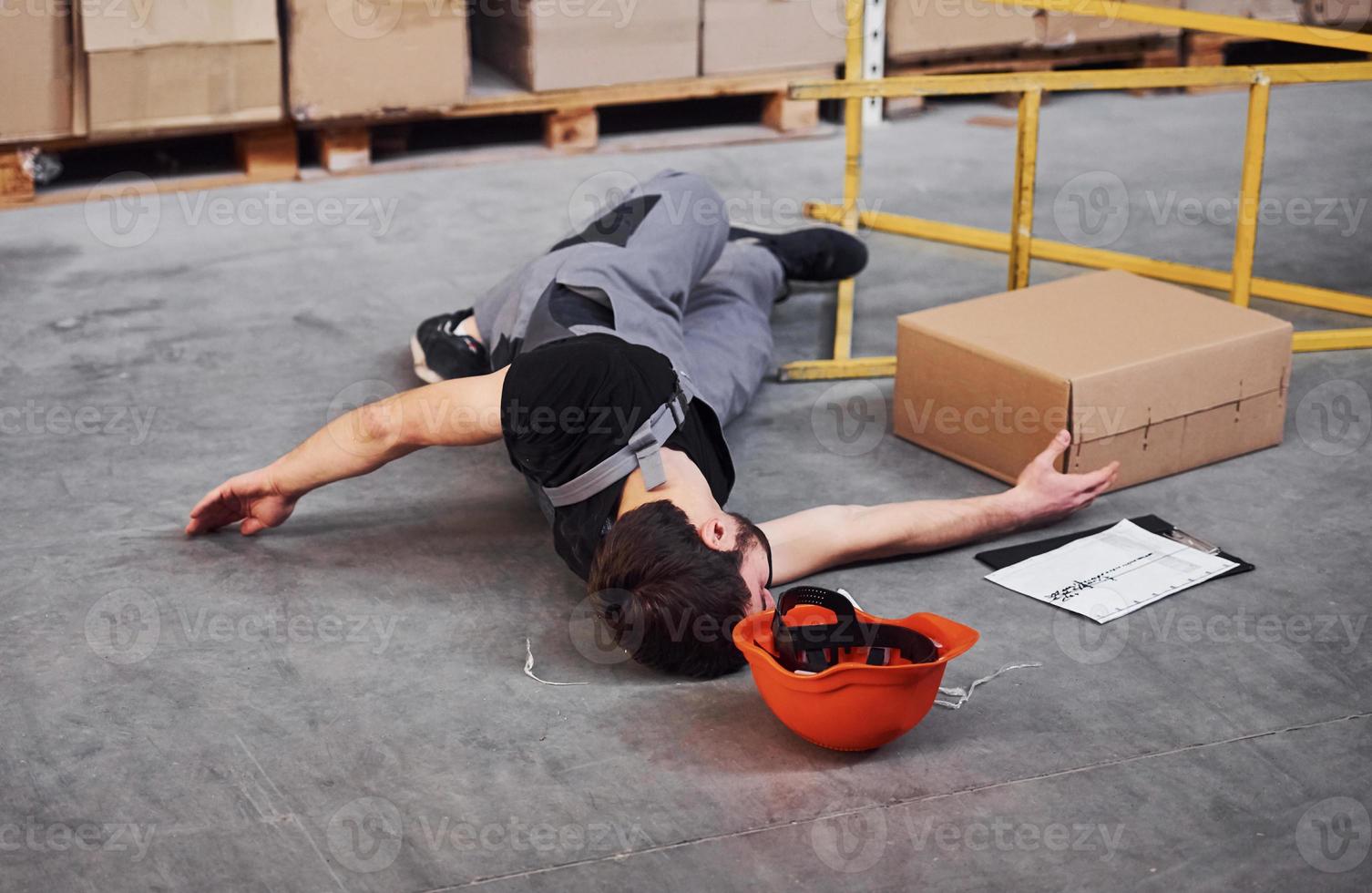 Warehouse worker after an accident in the storage. Man in uniform lying down on the ground photo