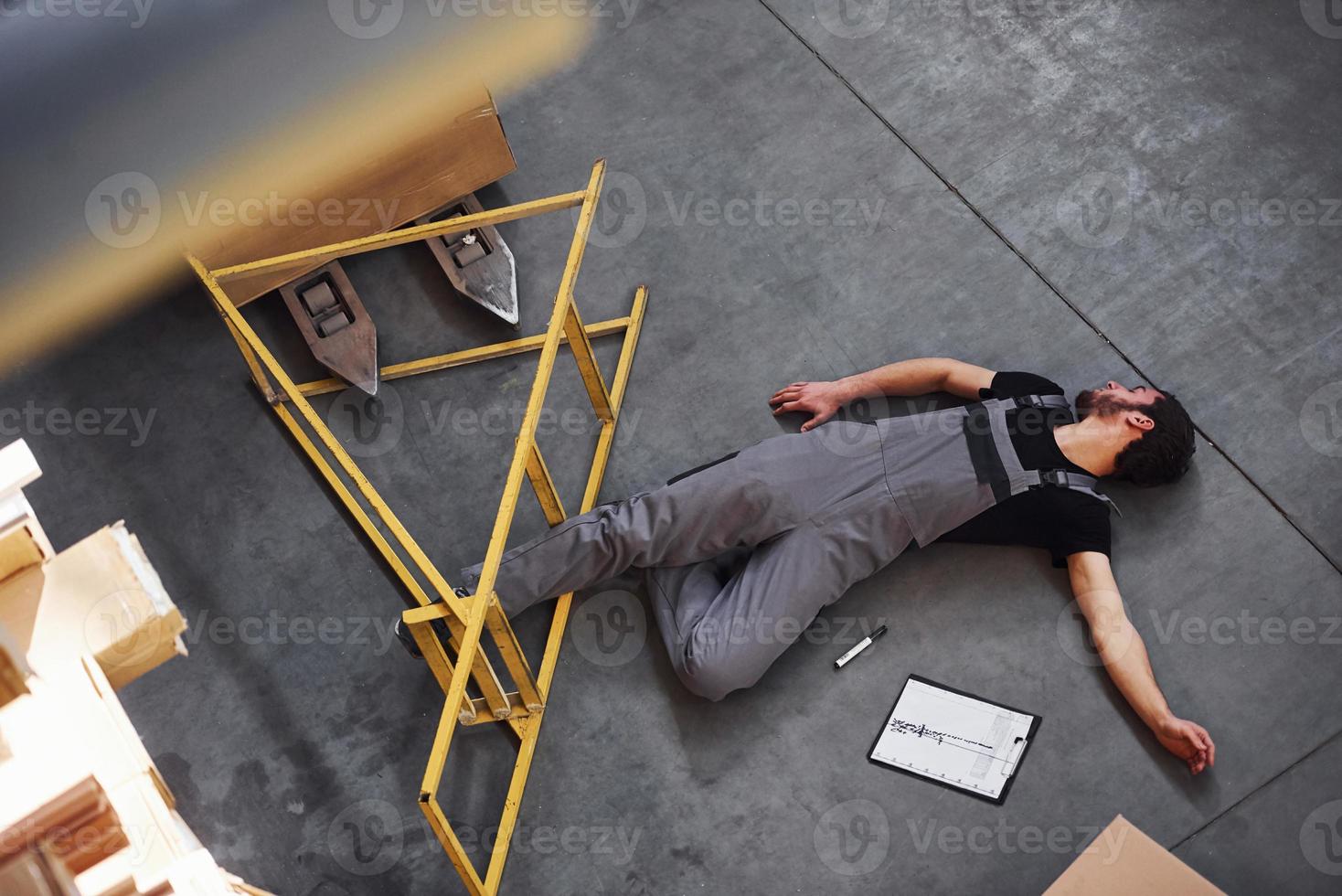 Warehouse worker after an accident in the storage. Man in uniform lying down on the ground photo