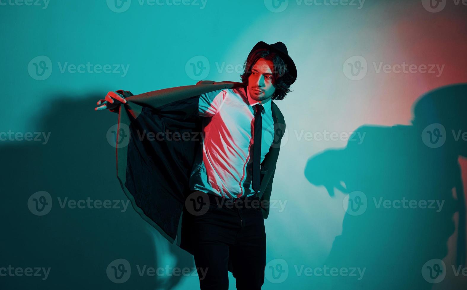 Portrait of young stylish man in hat, suit and tie that stands in neon lights in the studio photo