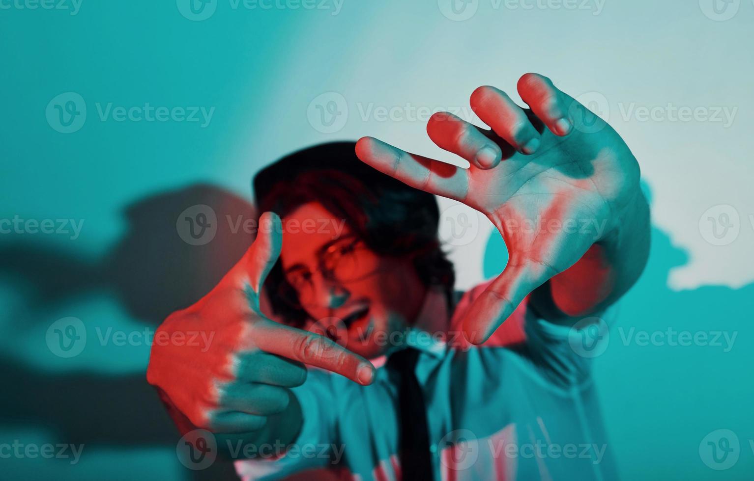 Portrait of young stylish man in hat and with glasses that stands in neon lights in the studio photo