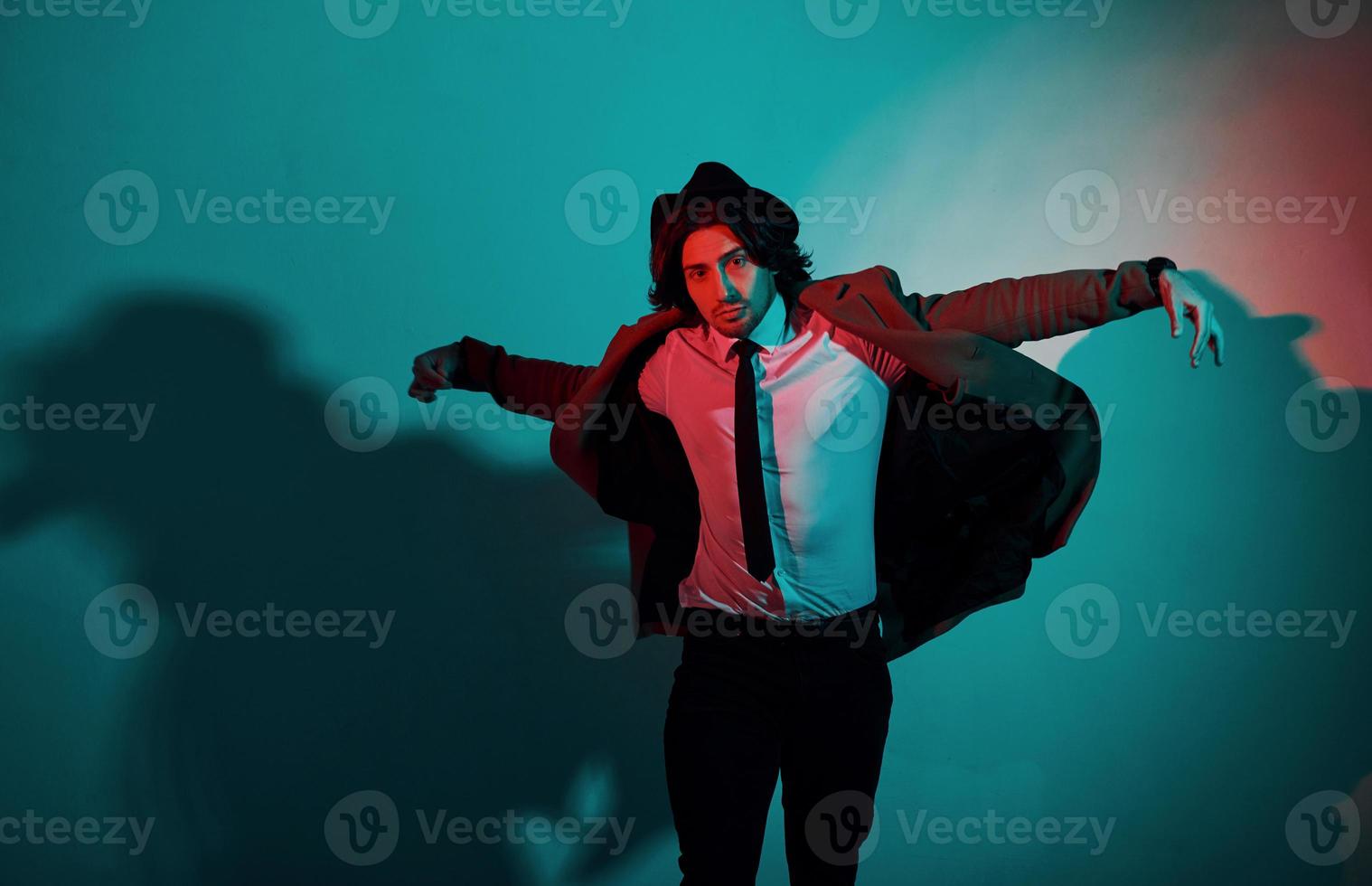 Portrait of young stylish man in hat, suit and tie that stands in neon lights in the studio photo