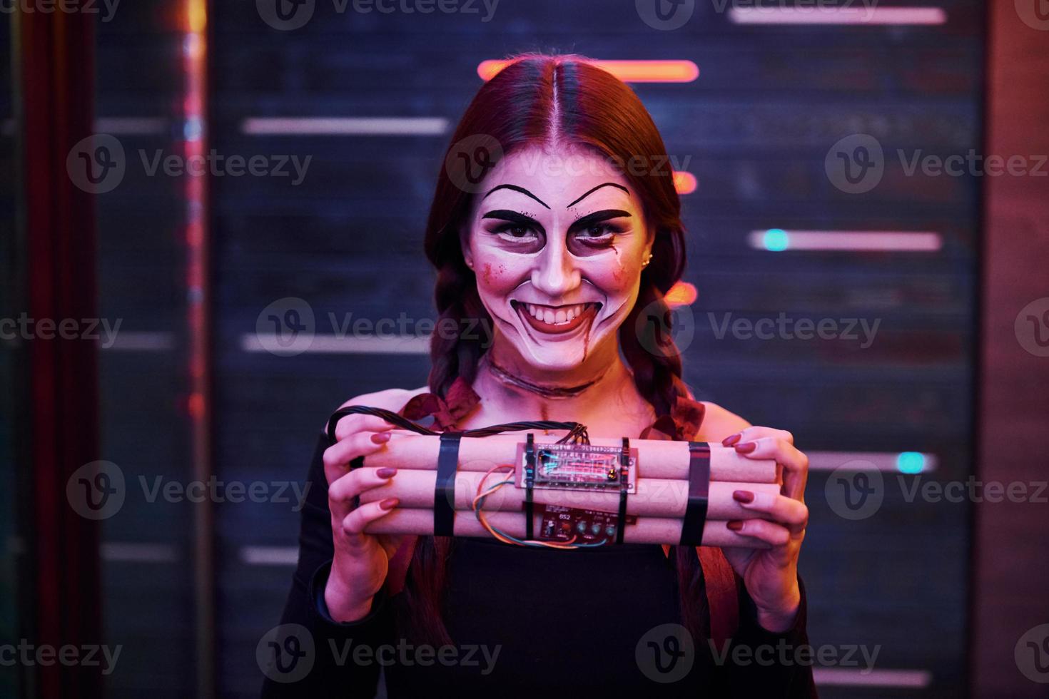 Portrait of woman that is on the thematic halloween party in scary makeup and costume with bomb in hands photo