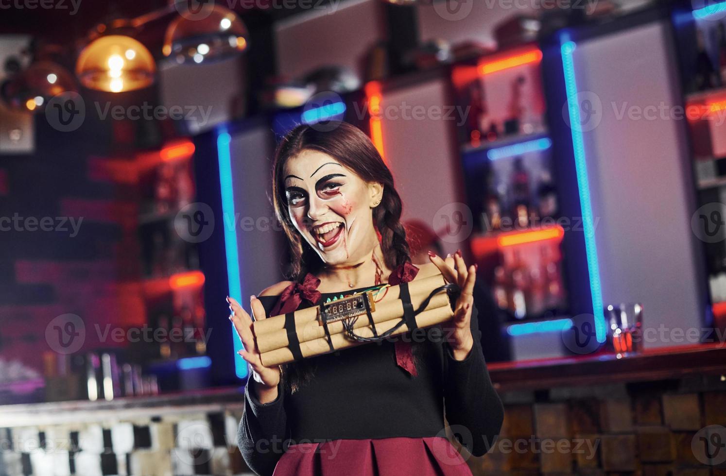 Portrait of woman that is on the thematic halloween party in scary makeup and costume with bomb in hands photo