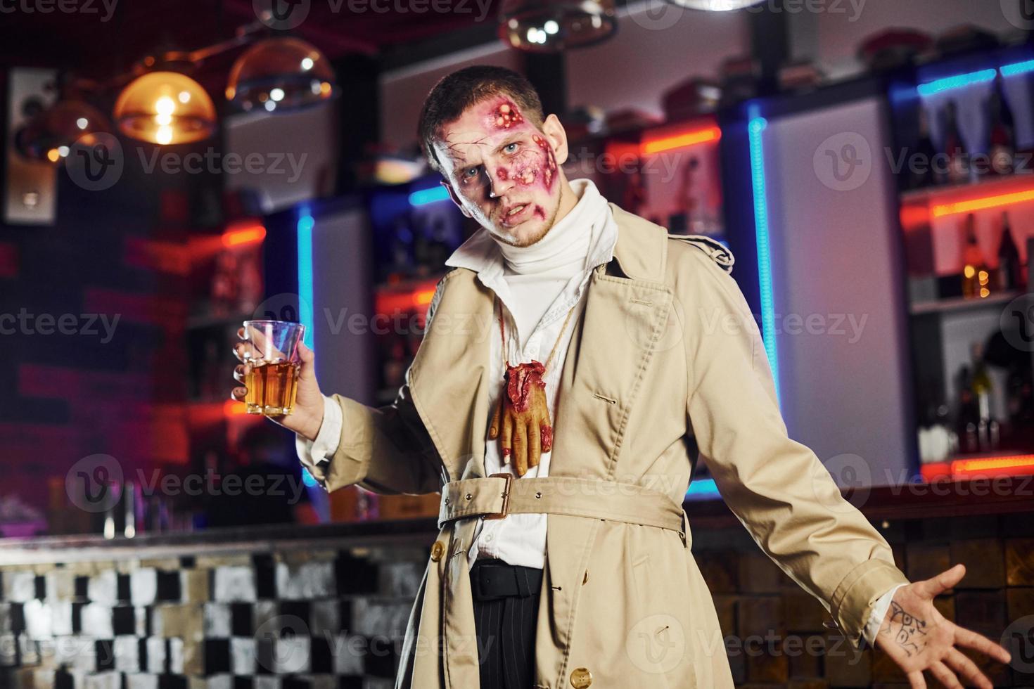 With drink in hand. Portrait of man that is on the thematic halloween party in zombie makeup and costume photo