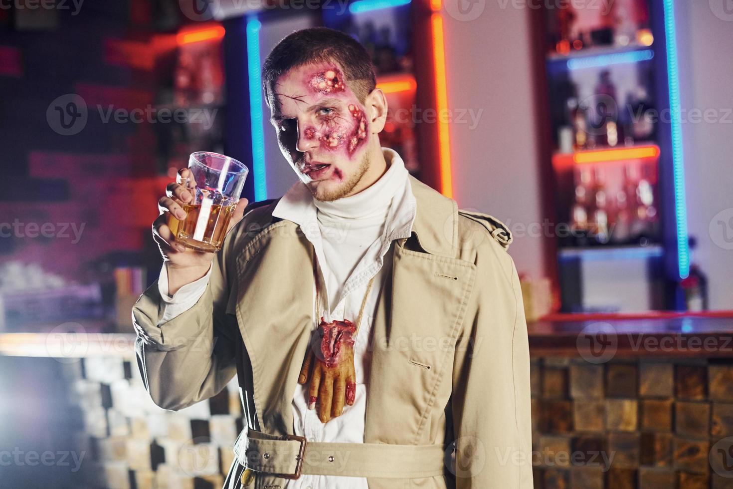 With drink in hand. Portrait of man that is on the thematic halloween party in zombie makeup and costume photo