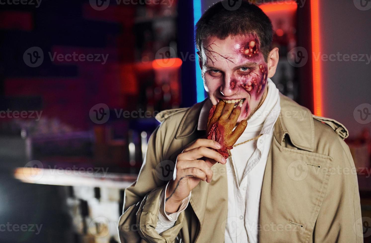 Eating dead hand. Portrait of man that is on the thematic halloween party in zombie makeup and costume photo