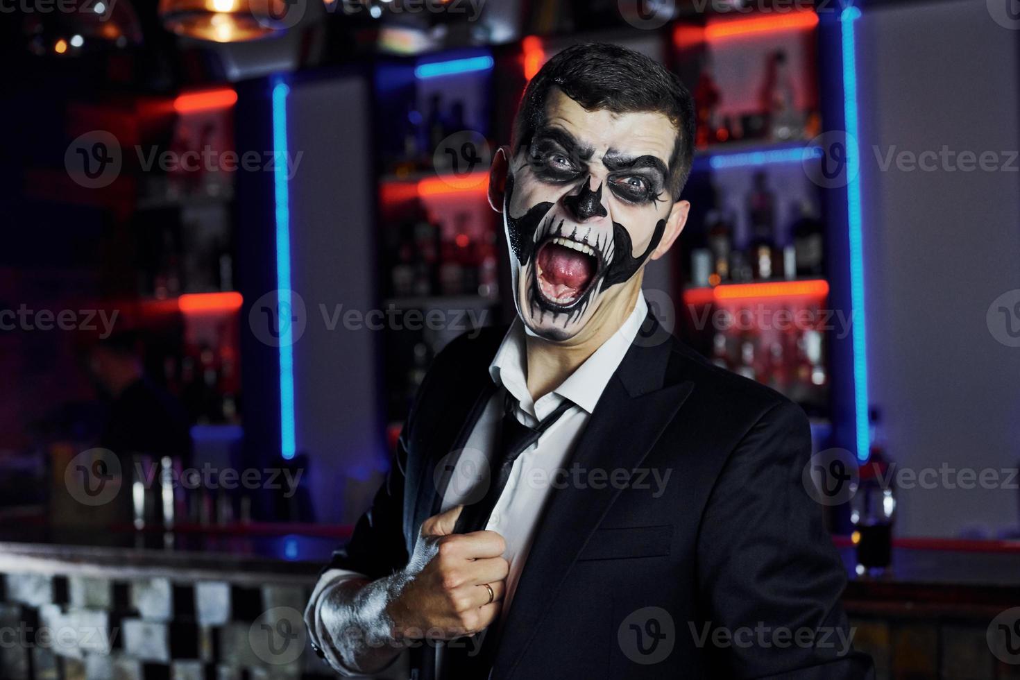 Screaming to the camera. Portrait of man that is on the thematic halloween party in scary skeleton makeup and costume photo