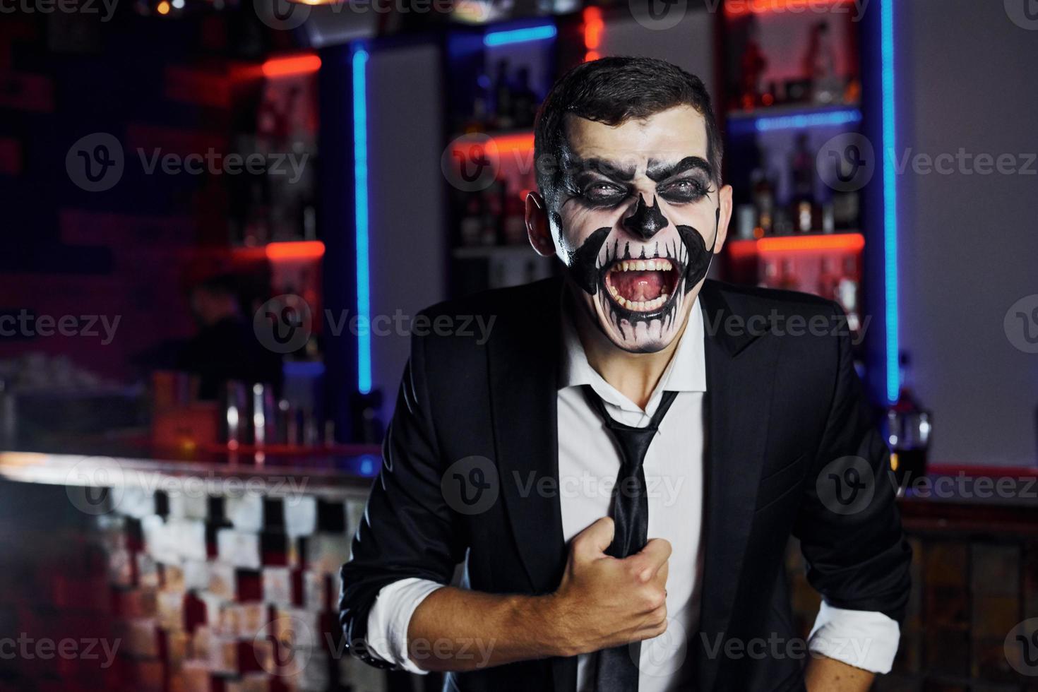 Screaming to the camera. Portrait of man that is on the thematic halloween party in scary skeleton makeup and costume photo