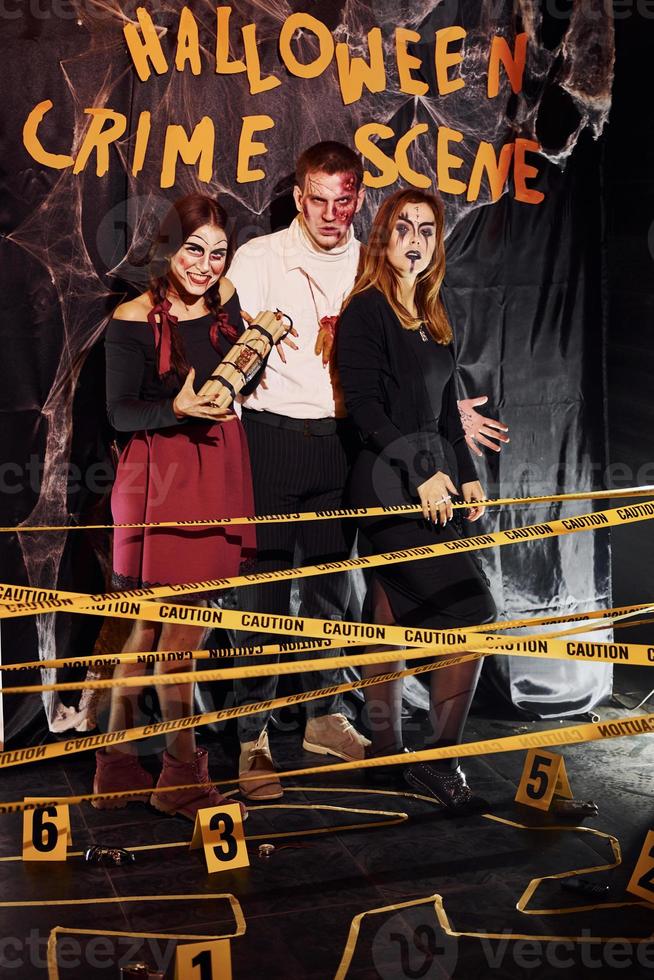 Standing against crime scene wall. Friends is on the thematic halloween party in scary makeup and costumes photo