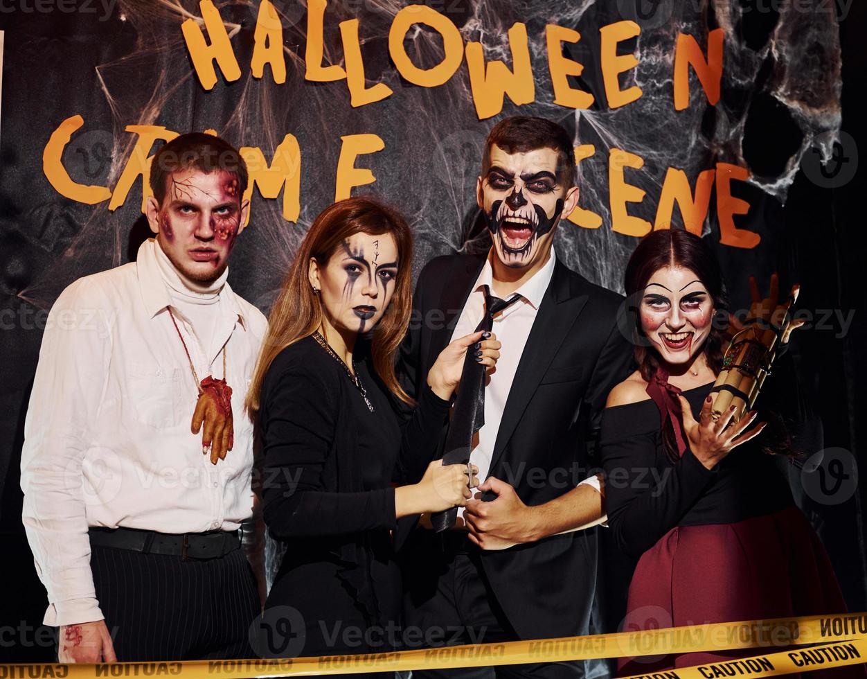 Standing against crime scene wall. Friends is on the thematic halloween party in scary makeup and costumes photo