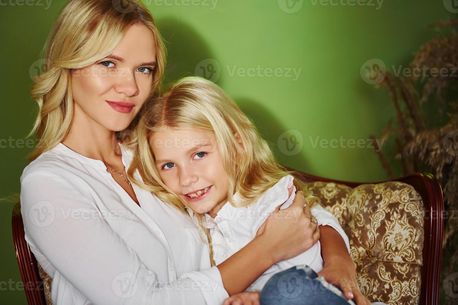 Mother with her daughter together in the studio with green background embracing each other photo