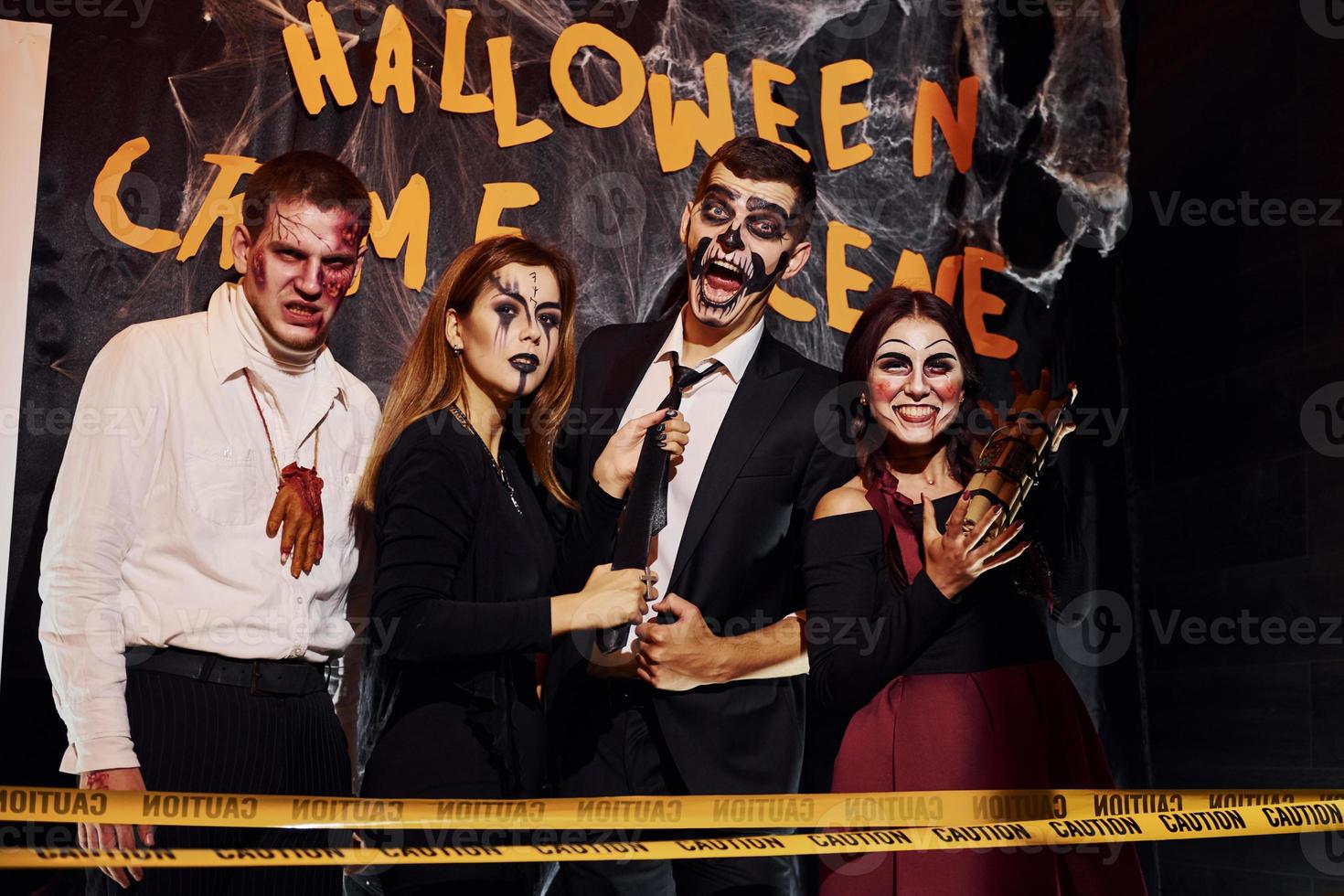 Standing against crime scene wall. Friends is on the thematic halloween party in scary makeup and costumes photo