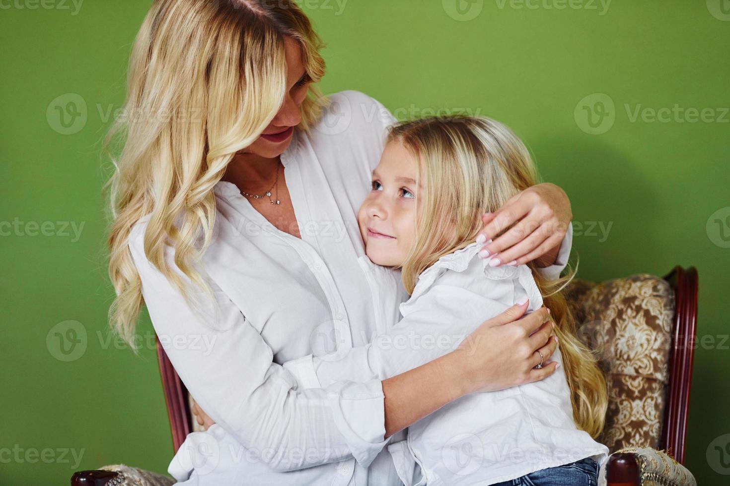 Mother with her daughter together in the studio with green background embracing each other photo