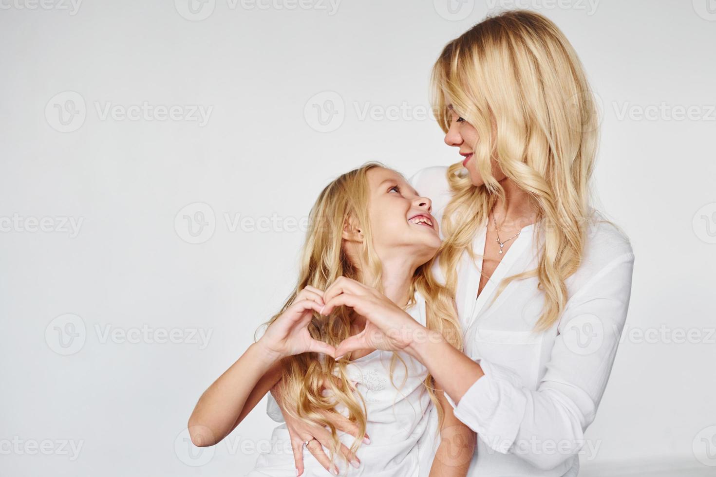 Mother with her daughter together shows love gesture in the studio with white background photo