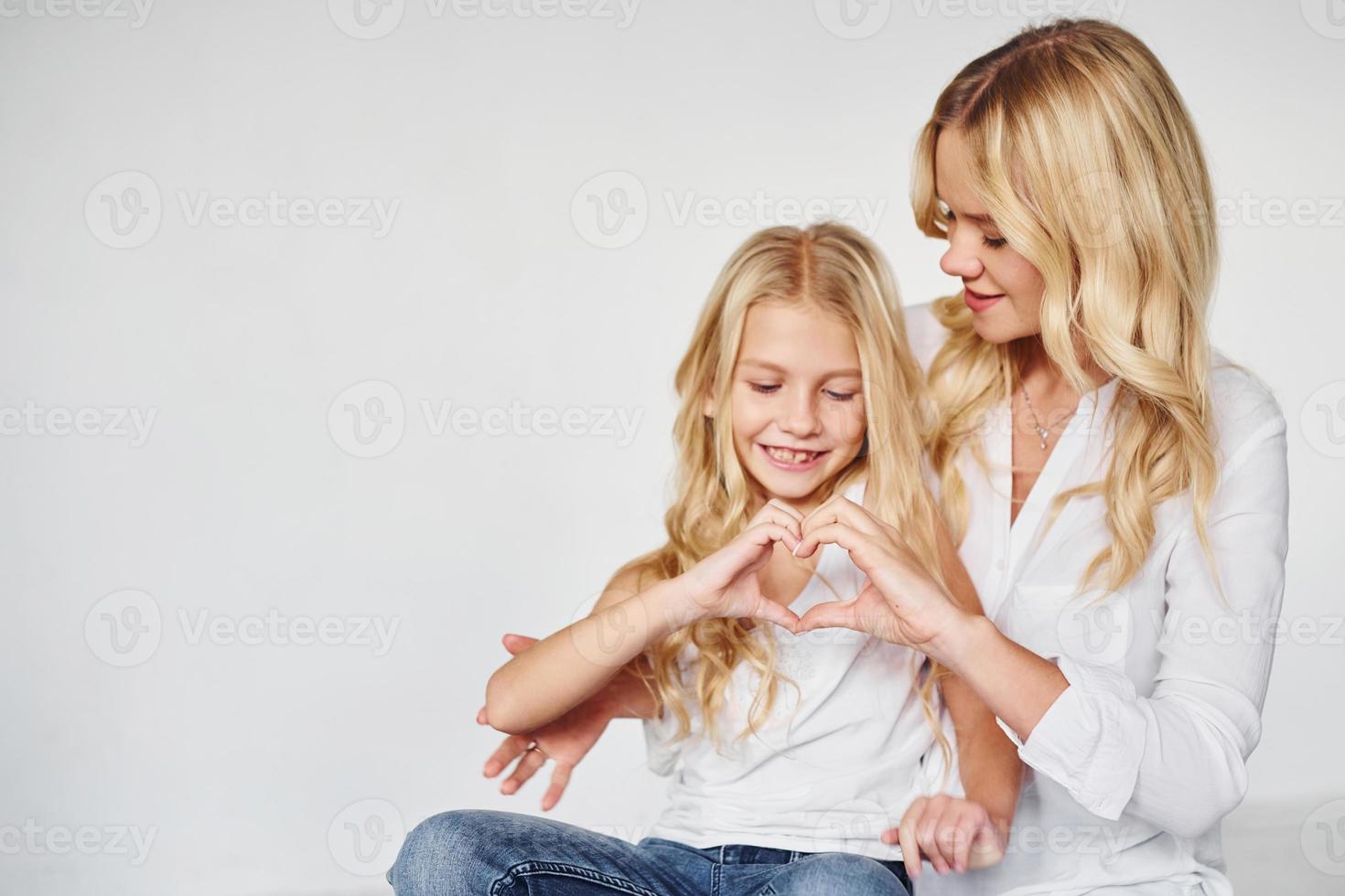 madre con su hija juntas muestra un gesto de amor en el estudio con fondo blanco foto