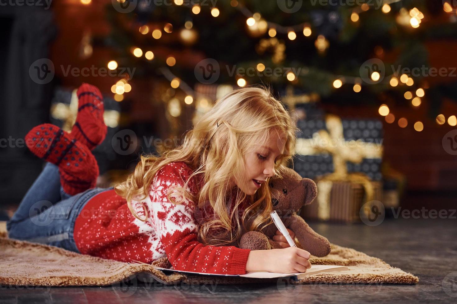 Cute little girl in red festive sweater lying down with teddy bear indoors celebrating new year photo