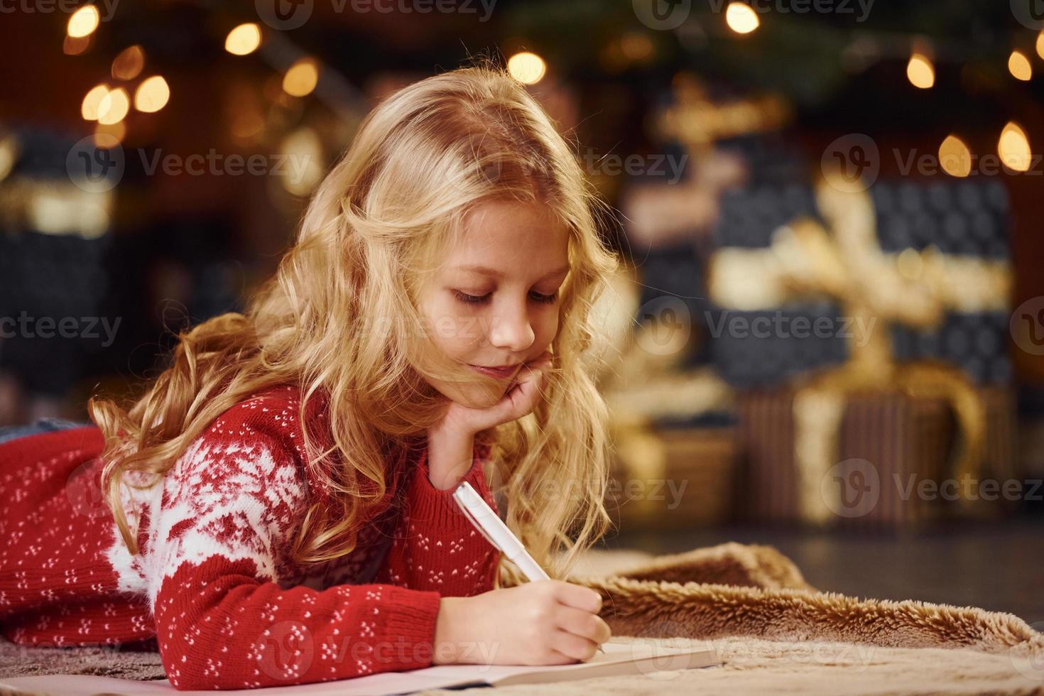 Cute little girl in red festive sweater indoors lying down celebrating new year and christmas holidays photo