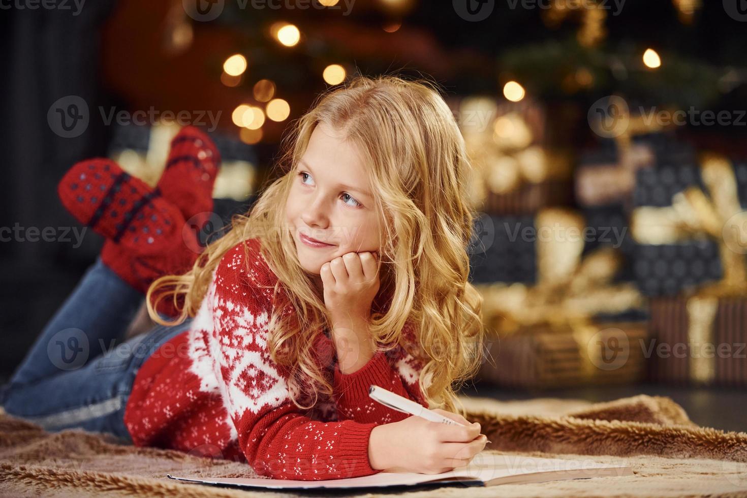 Cute little girl in red festive sweater indoors lying down celebrating new year and christmas holidays photo
