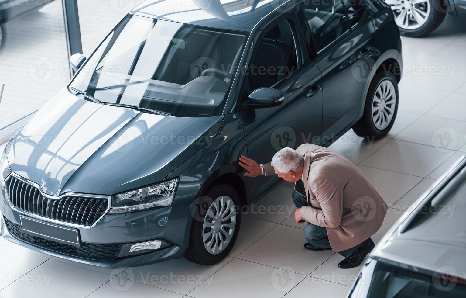 Aged man in formal wear walking in the automobile salon and looking for the car photo