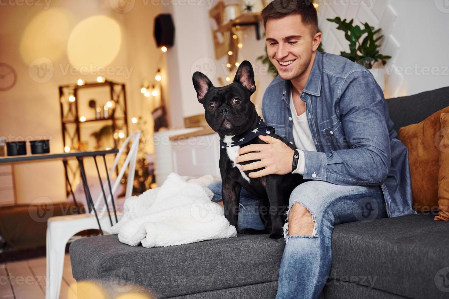 Smiling man in jeans sitting in the sofa at home with his cute dog photo