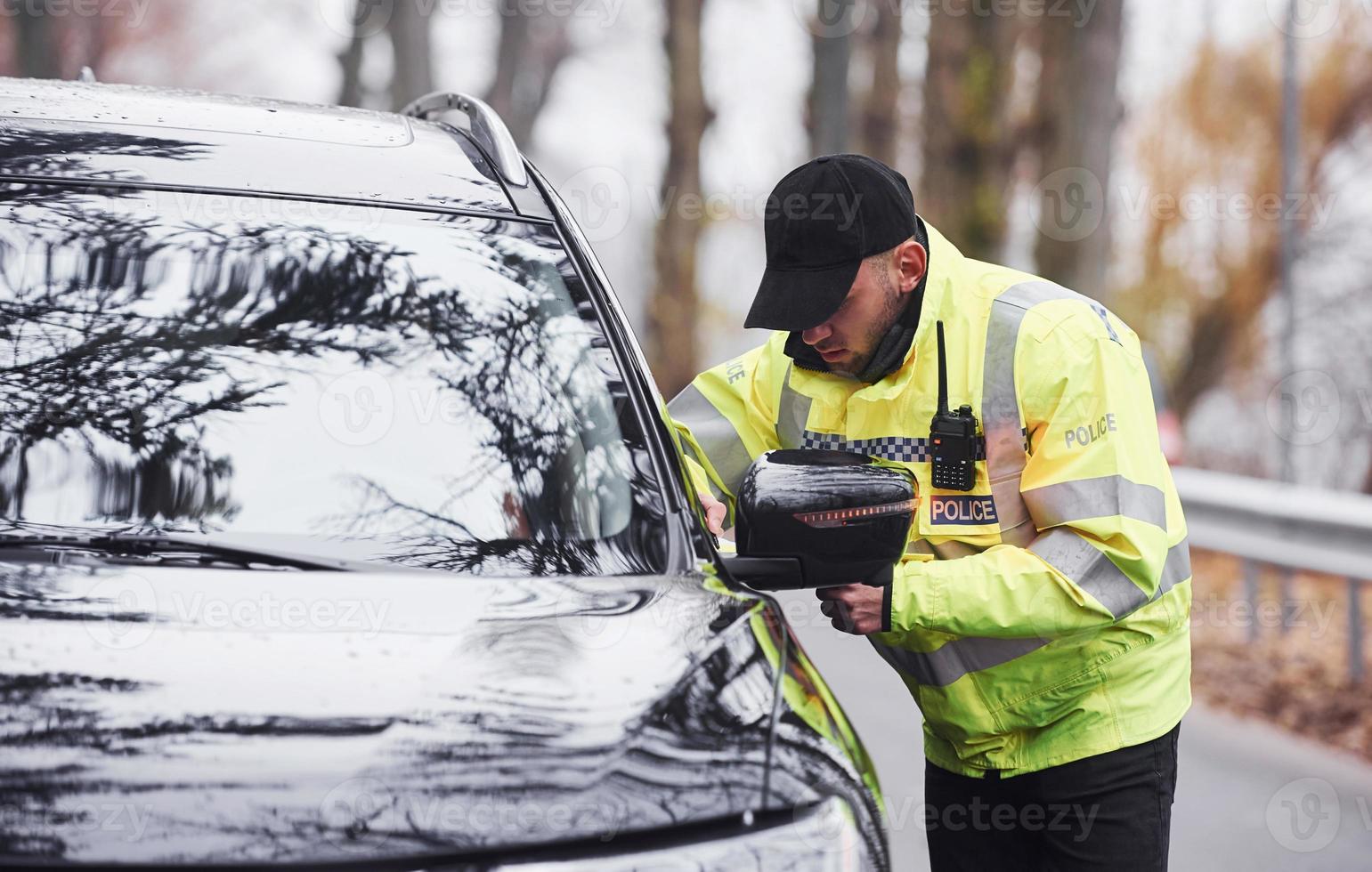 Male police officer in green uniform checking vehicle on the road photo