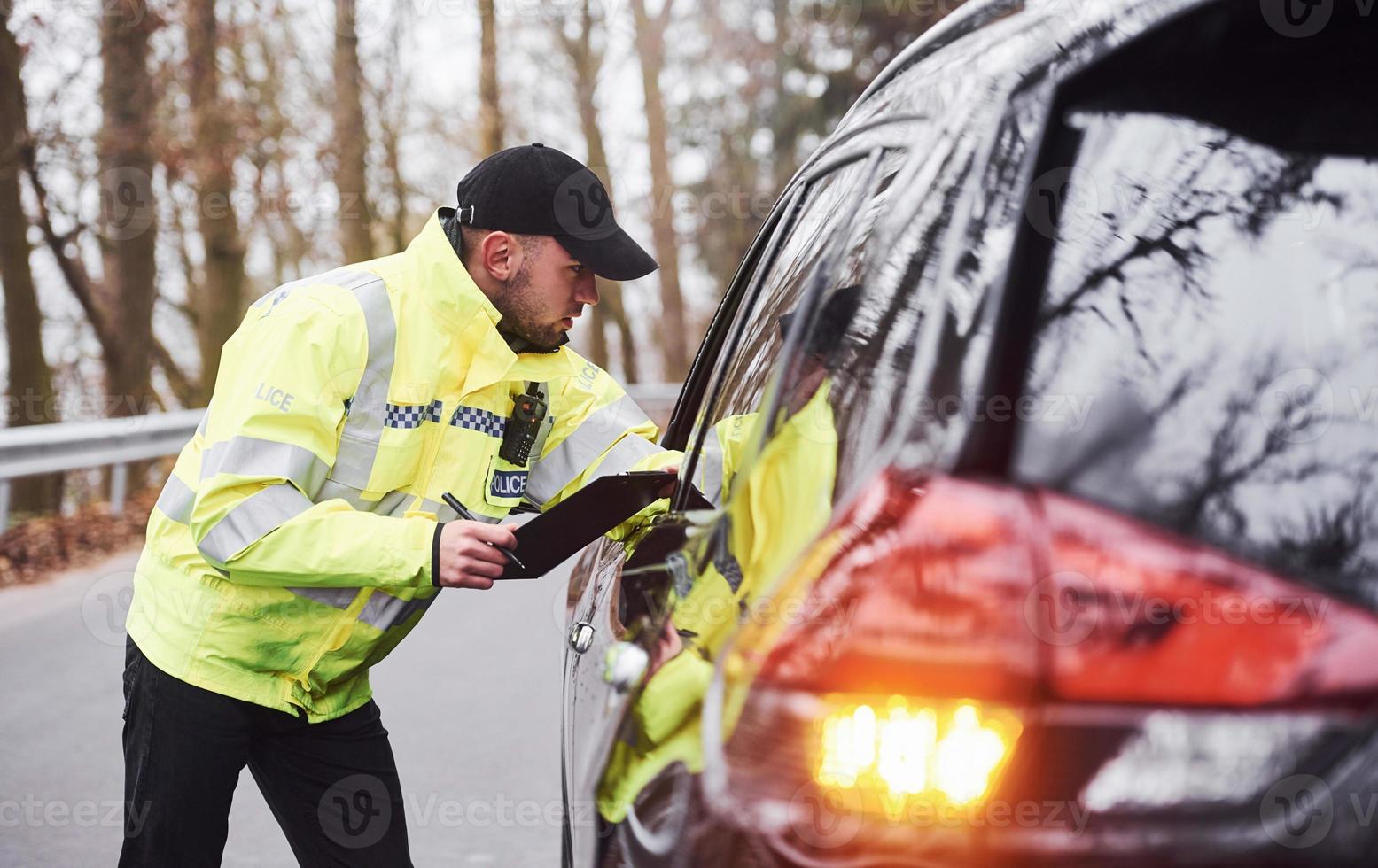 Male police officer in green uniform checking vehicle on the road photo