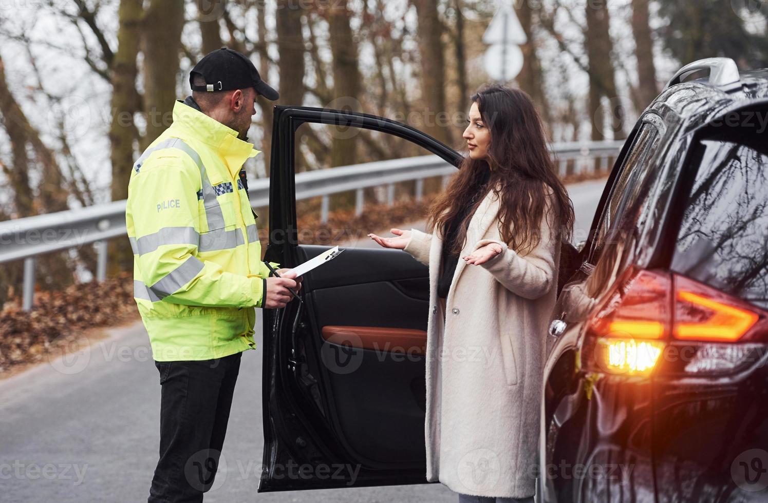 Male police officer in green uniform talking with female owner of the car on the road photo