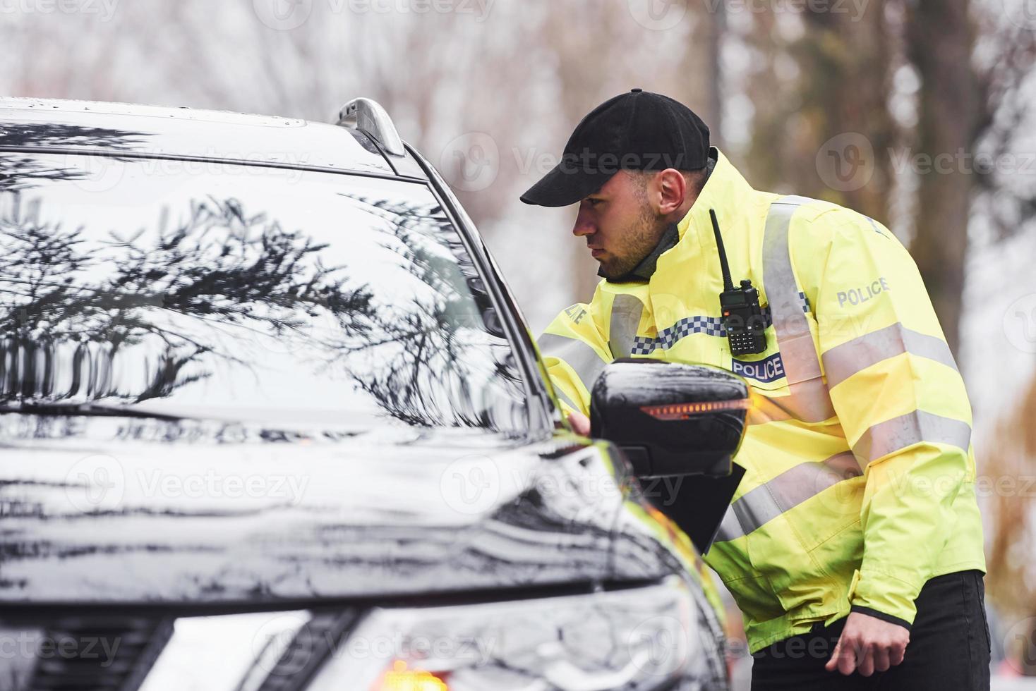Male police officer in green uniform checking vehicle on the road photo
