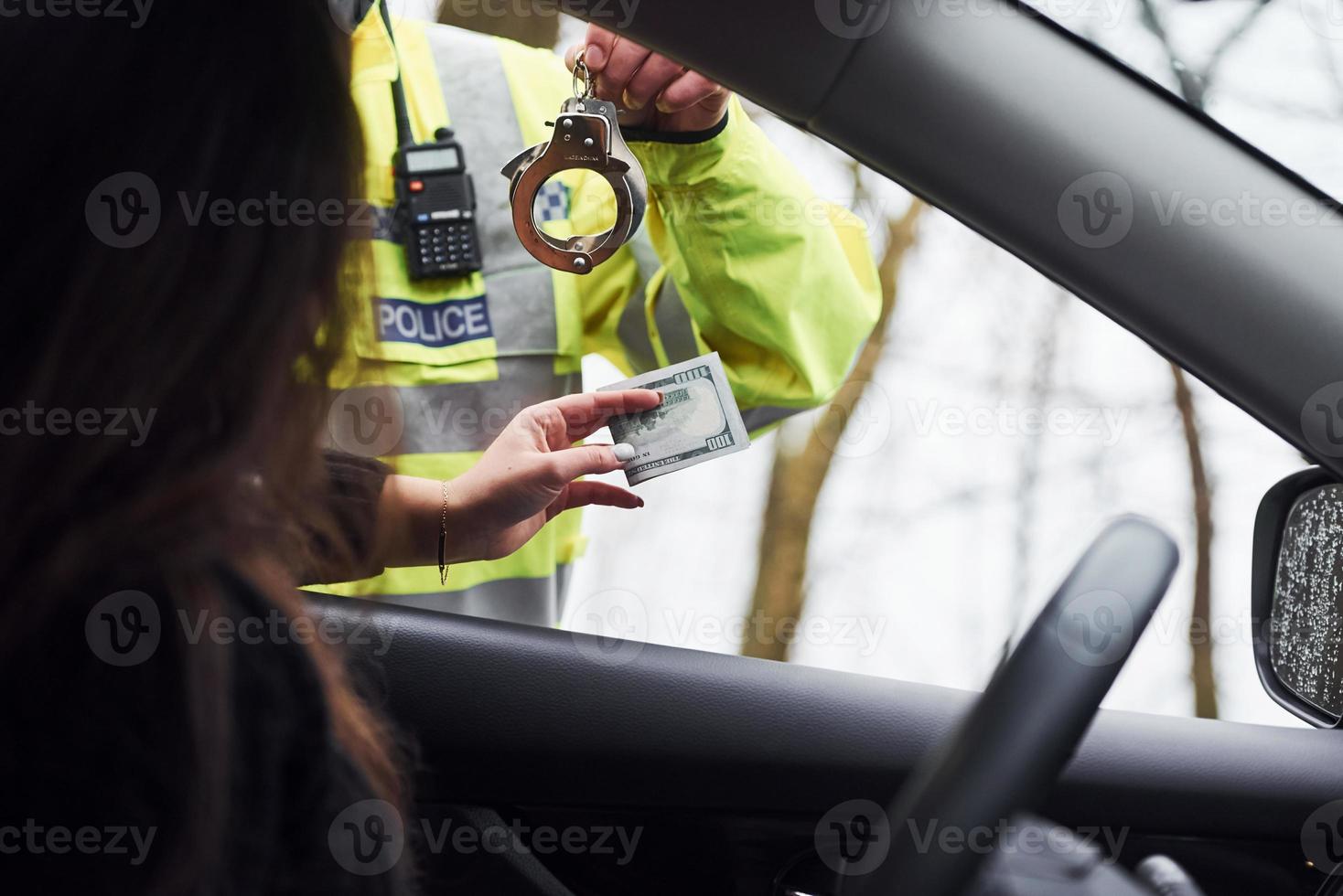 Male police officer in green uniform and with handcuffs refuse to take bribe from woman in vehicle photo