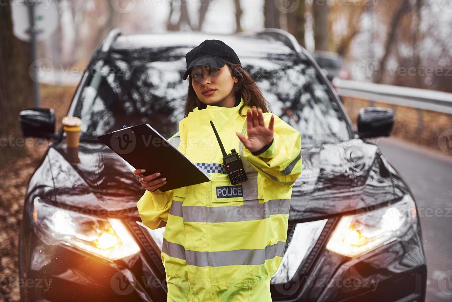 Female police officer in green uniform standing with radio transmitter and notepad against car photo