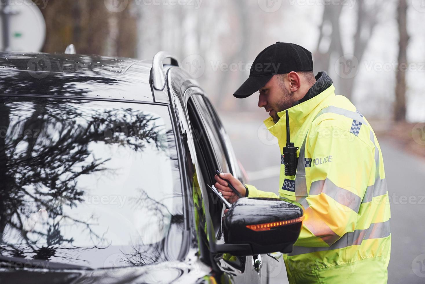 Male police officer in green uniform checking vehicle on the road photo