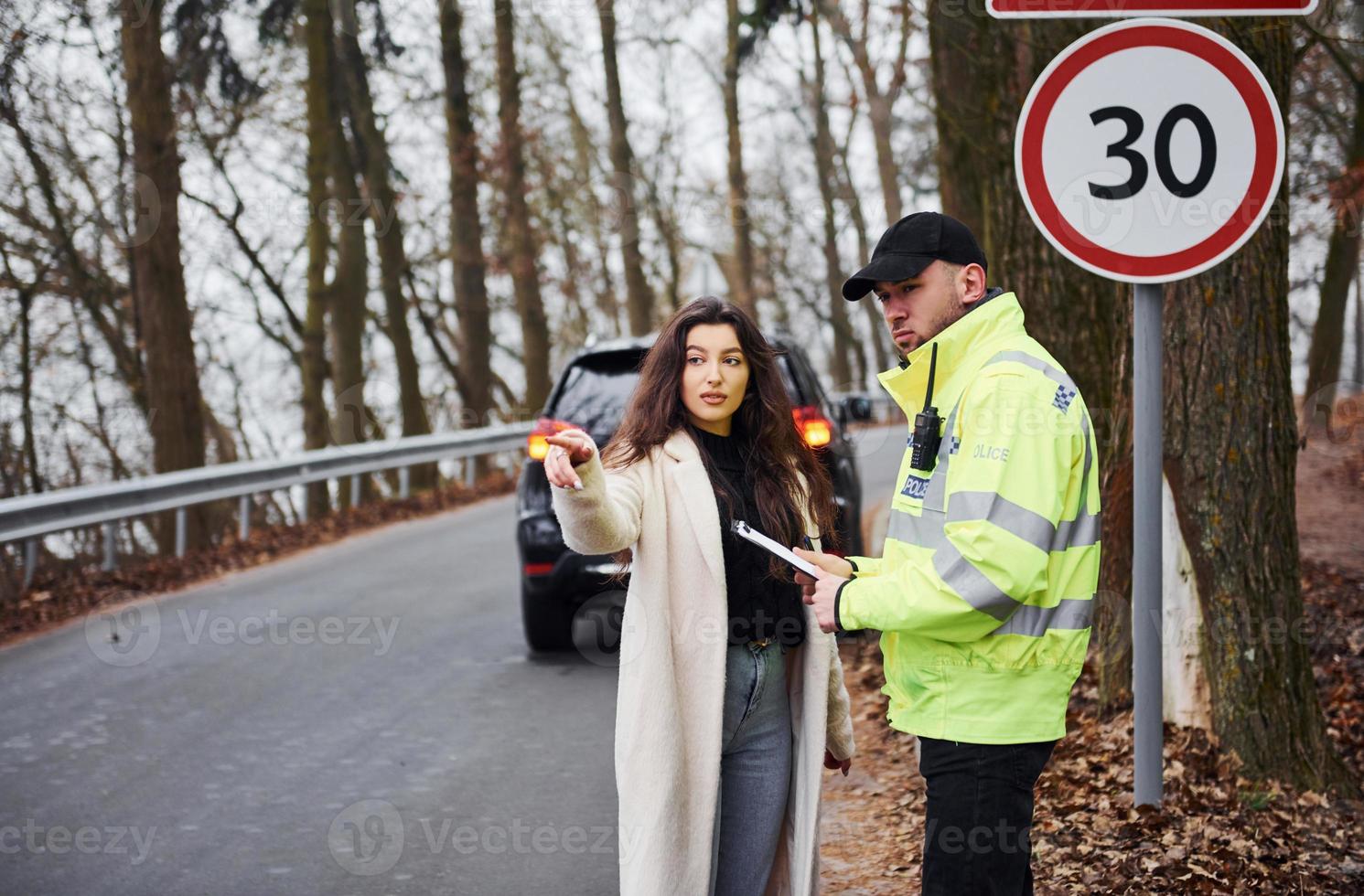 Male police officer in green uniform talking with female owner of the car on the road photo