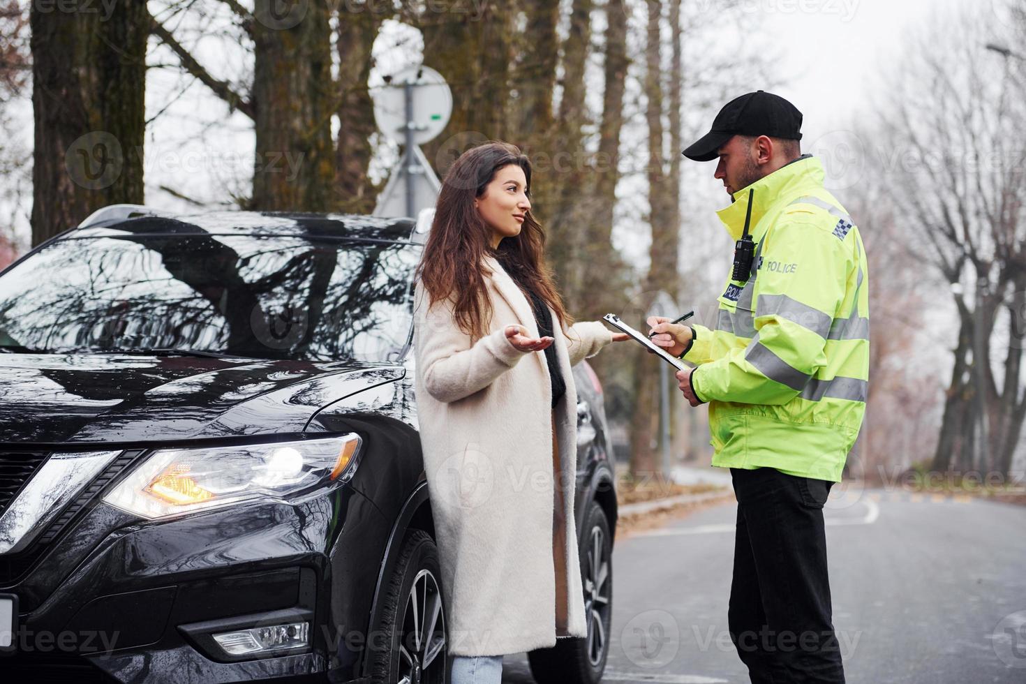 Male police officer in green uniform talking with female owner of the car on the road photo