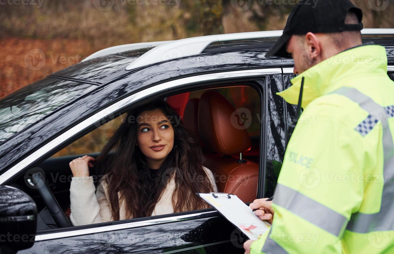 Male police officer in green uniform with notepad checking vehicle on the road photo